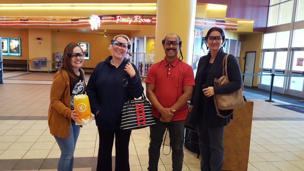 Members of the closed captioning team wearing closed captioning glasses at a local movie theater