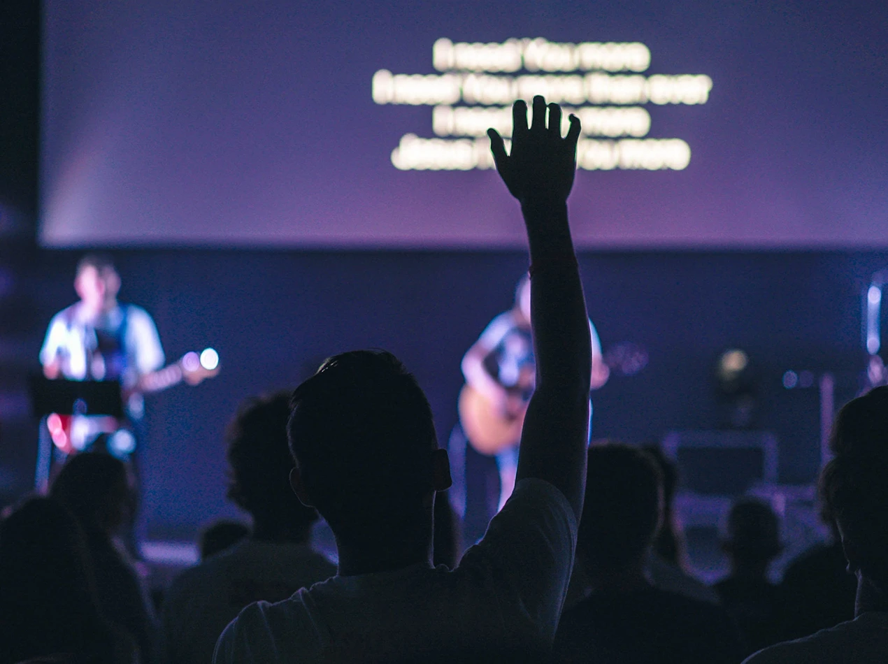 Photo of attendees participating in worship services, with captioning on the stage screen