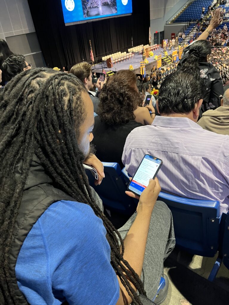 Guest at a UC Irvine commencement ceremony using a smartphone to access live captions and multilingual translation while watching the graduation ceremony.